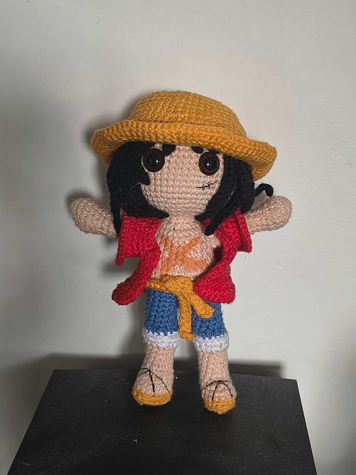 L'amigurumi de Monkey D. Luffy terminé, debout sur un support noir, les bras écartés