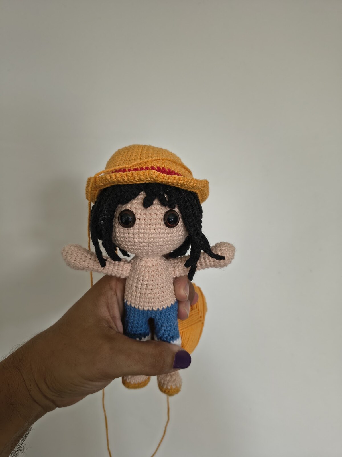 Travail en cours : l'amigurumi avec ses cheveux en laine noire, ses yeux de sécurité et ses bras fixés, coiffé du chapeau mais sans gilet
