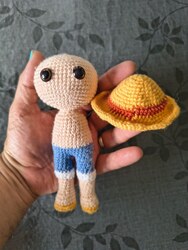 Travail en cours : un corps d'amigurumi nu en laine chair avec un short bleu, tenu à côté du chapeau de paille terminé