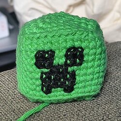 Gros plan d'un cube vert au crochet avec le visage du Creeper brodé en noir sur le devant